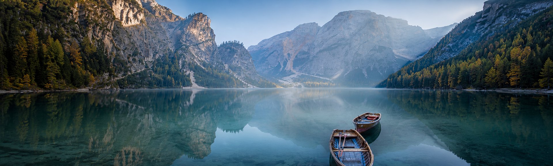 Still lake with rowing boats and mountain reflection